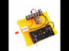 DIY Electronics STEM Kit mounted on a yellow perforated board with LED, potentiometer, battery holder, resistors, terminal block, and wires – hands-on circuit project for learning electricity and light experiments.